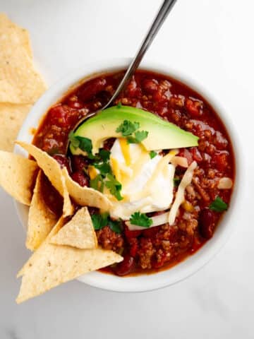 homemade chili in a bowl topped with sour cream, cheese, avocado, and chips.