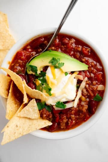 homemade chili in a bowl topped with sour cream, cheese, avocado, and chips.