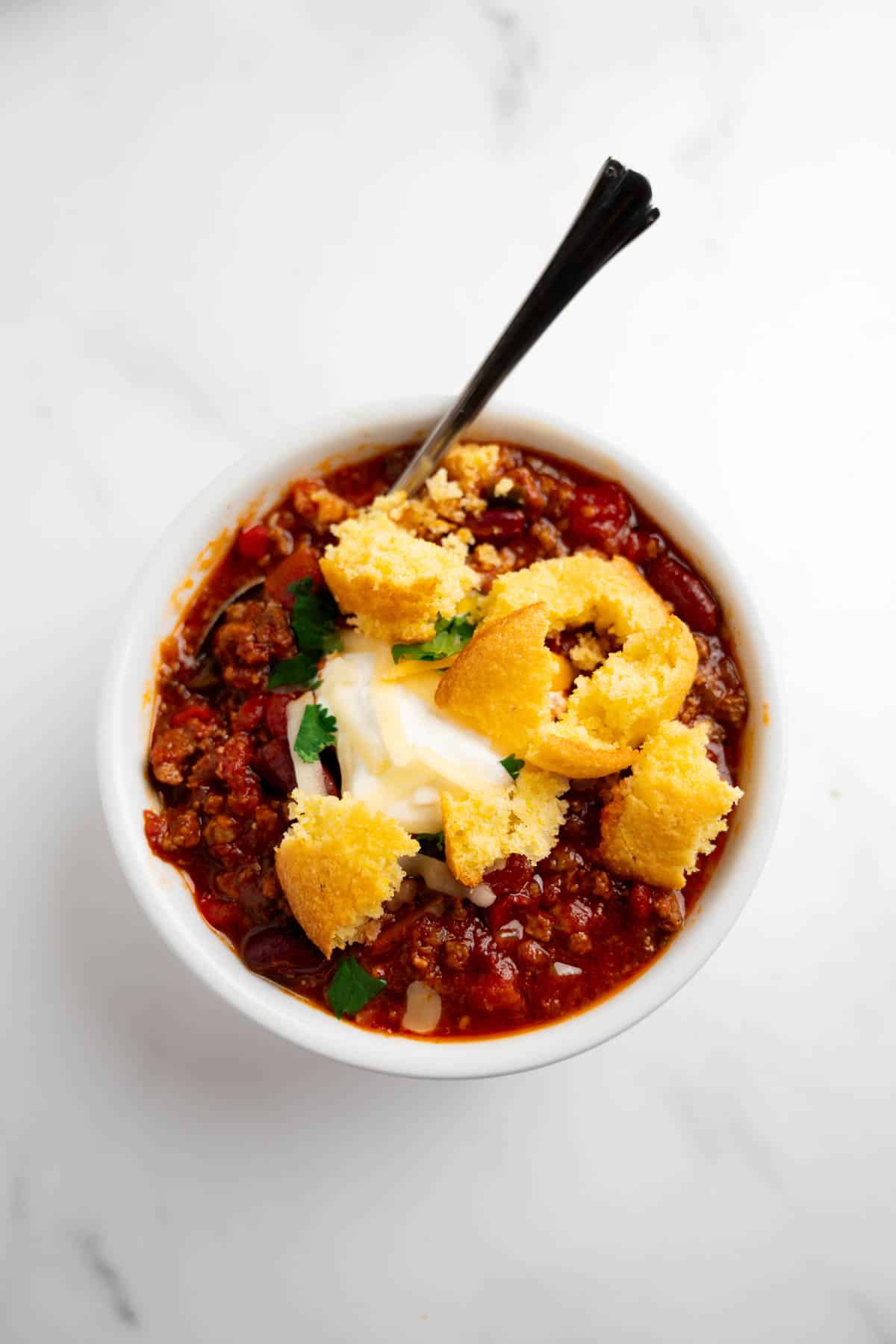 cornbread on top of a bowl of chili with a spoon.