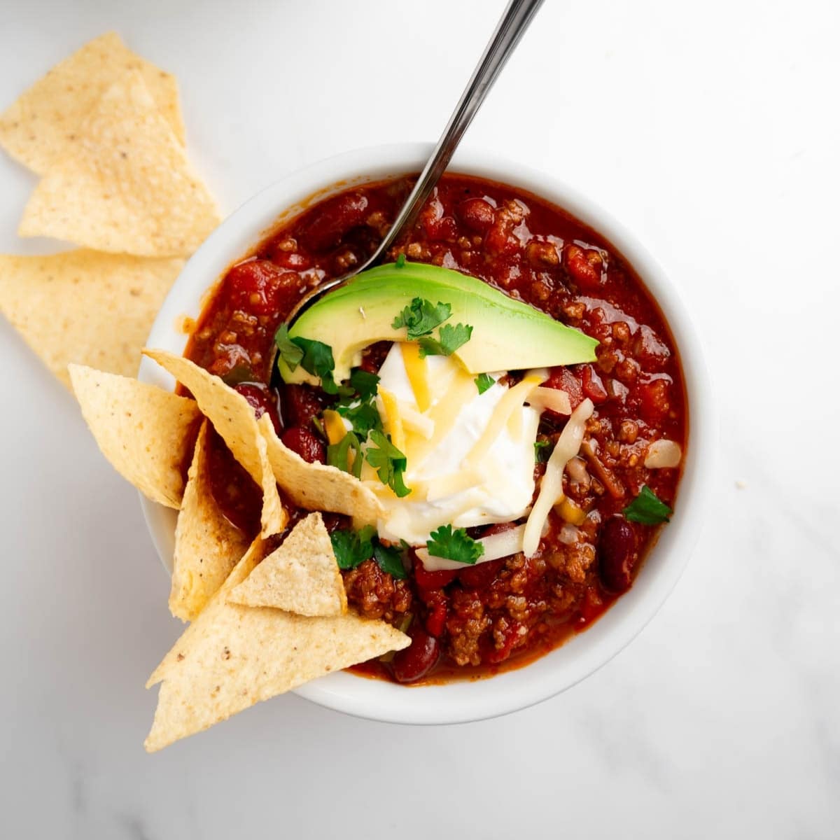 chili in a bowl topped with sour cream, cheese, and avocado.