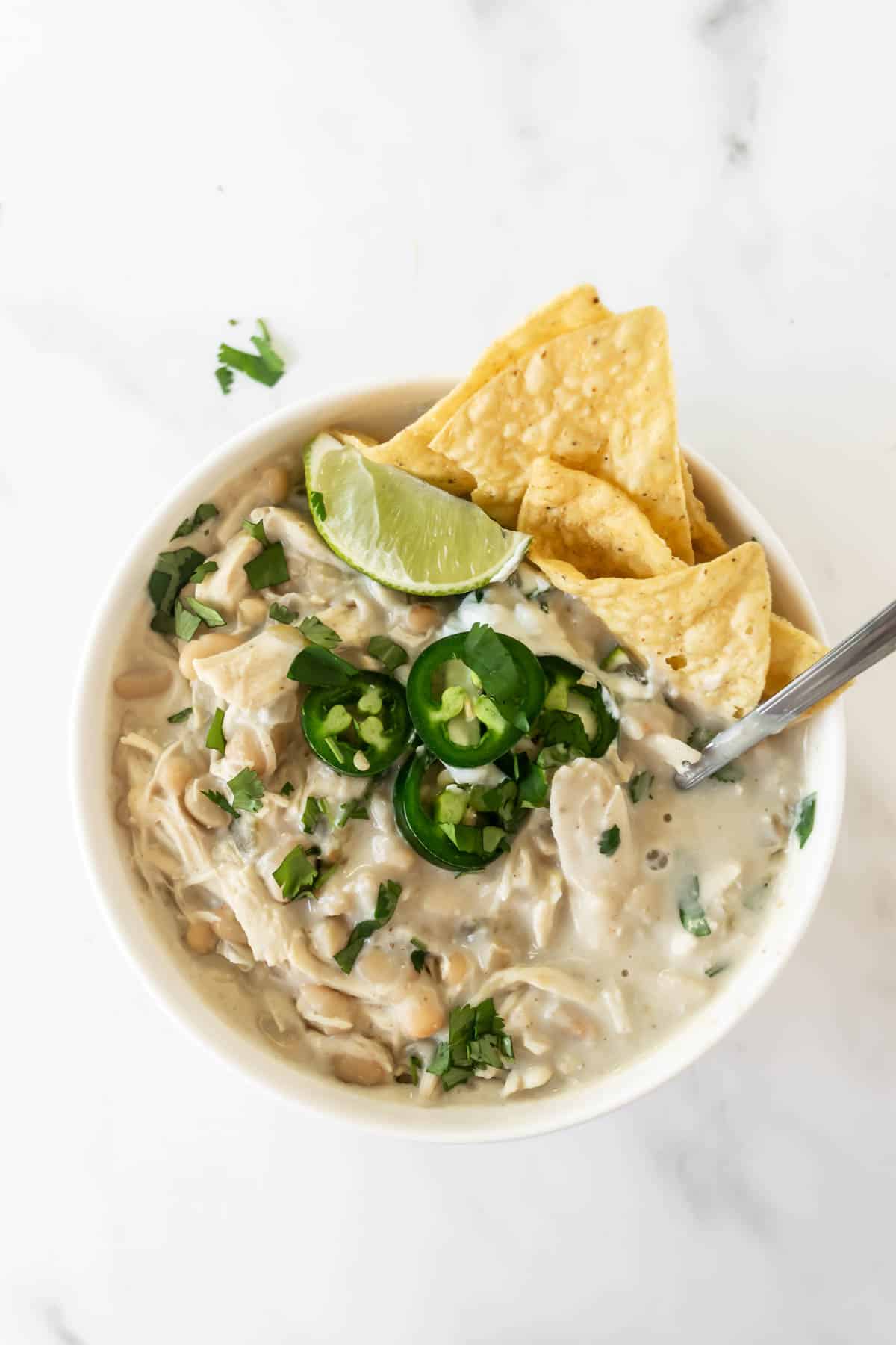 white chicken chili in a white bowl topped with jalapeños, lime, and chips.