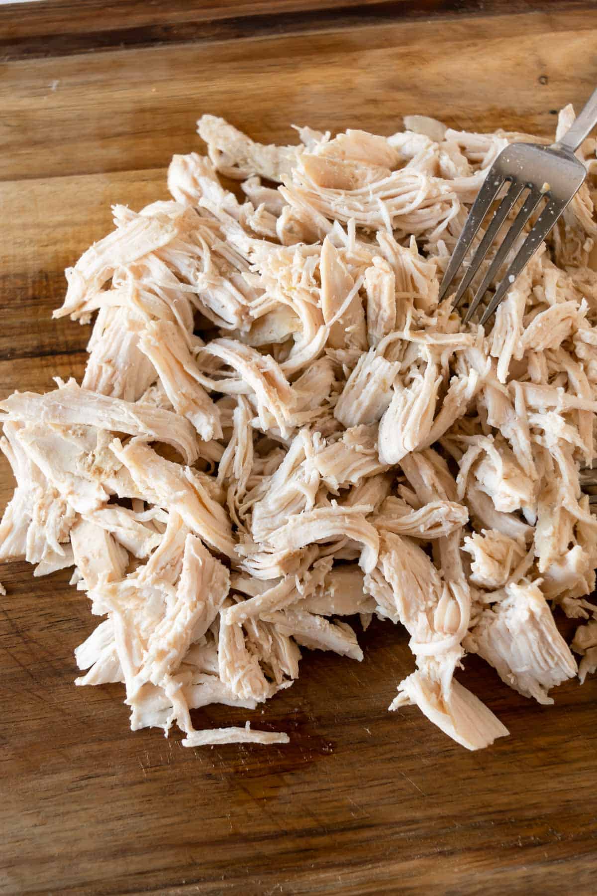 shredding chicken with a fork on a wood cutting board.