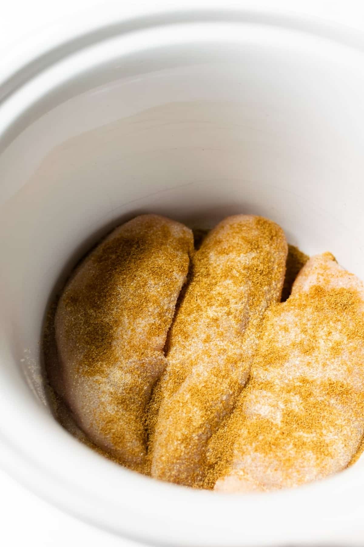 chicken breasts topped with spices in a slow cooker.