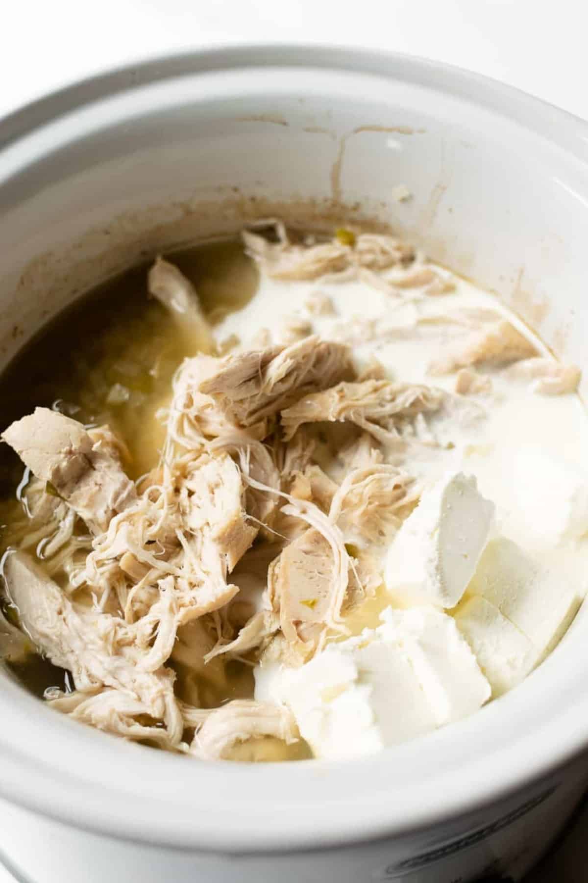 shredded chicken with cubed cream cheese in a slow cooker.