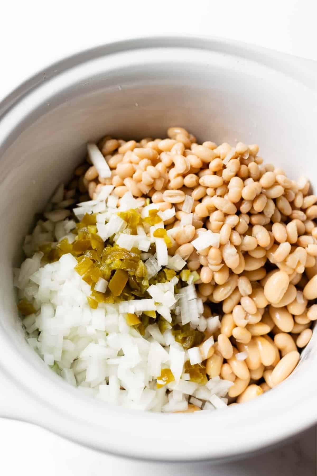 diced onions, jalapeños, and white beans in a slow cooker.