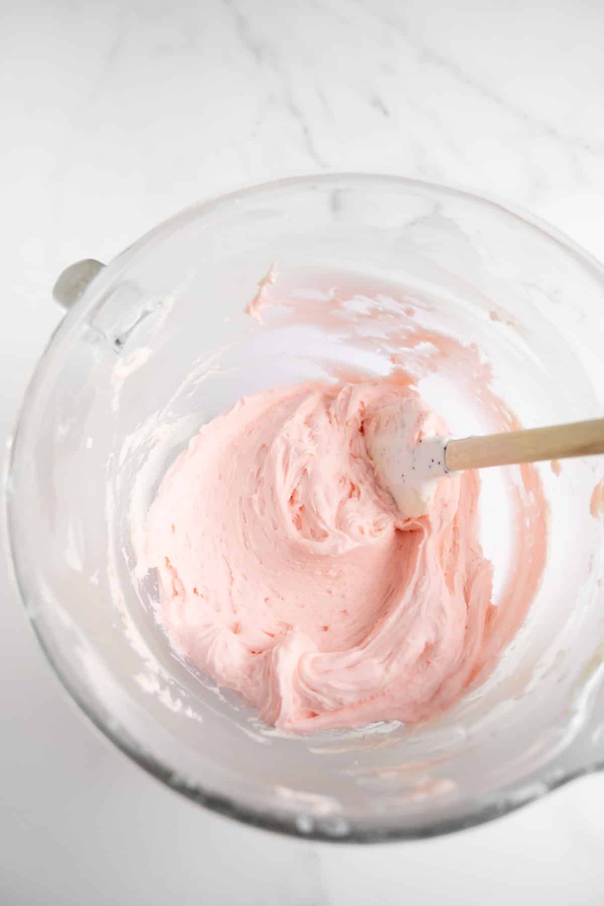 light pink buttercream frosting in a bowl with a spatula.