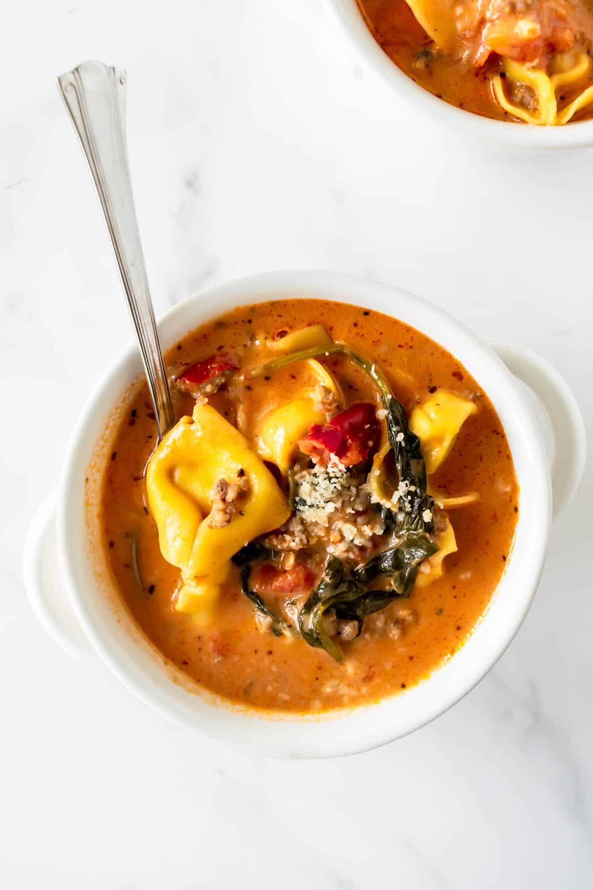 creamy tortellini soup with sausage in a white bowl with a spoon.