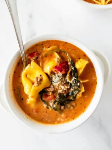 creamy tortellini soup in a white bowl topped with parmesan cheese.