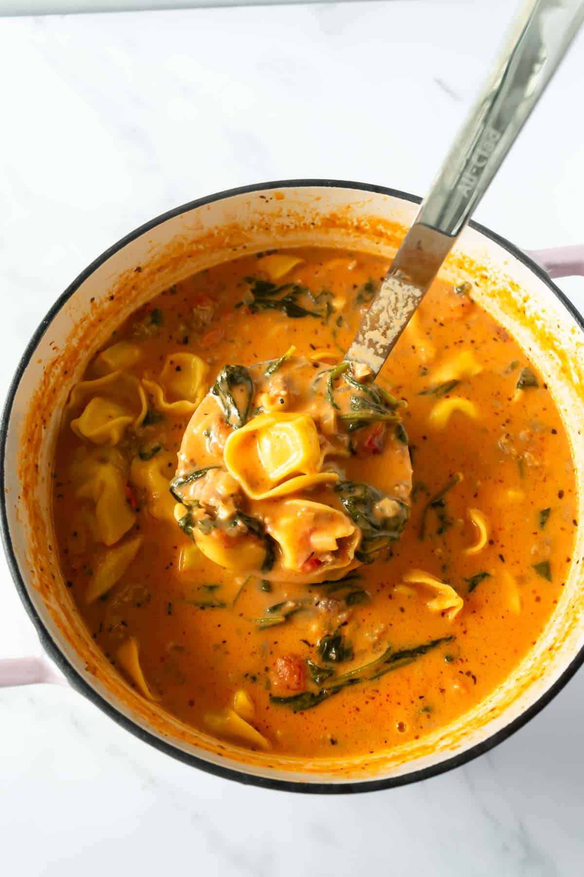 tortellini soup in a pot with a ladle.