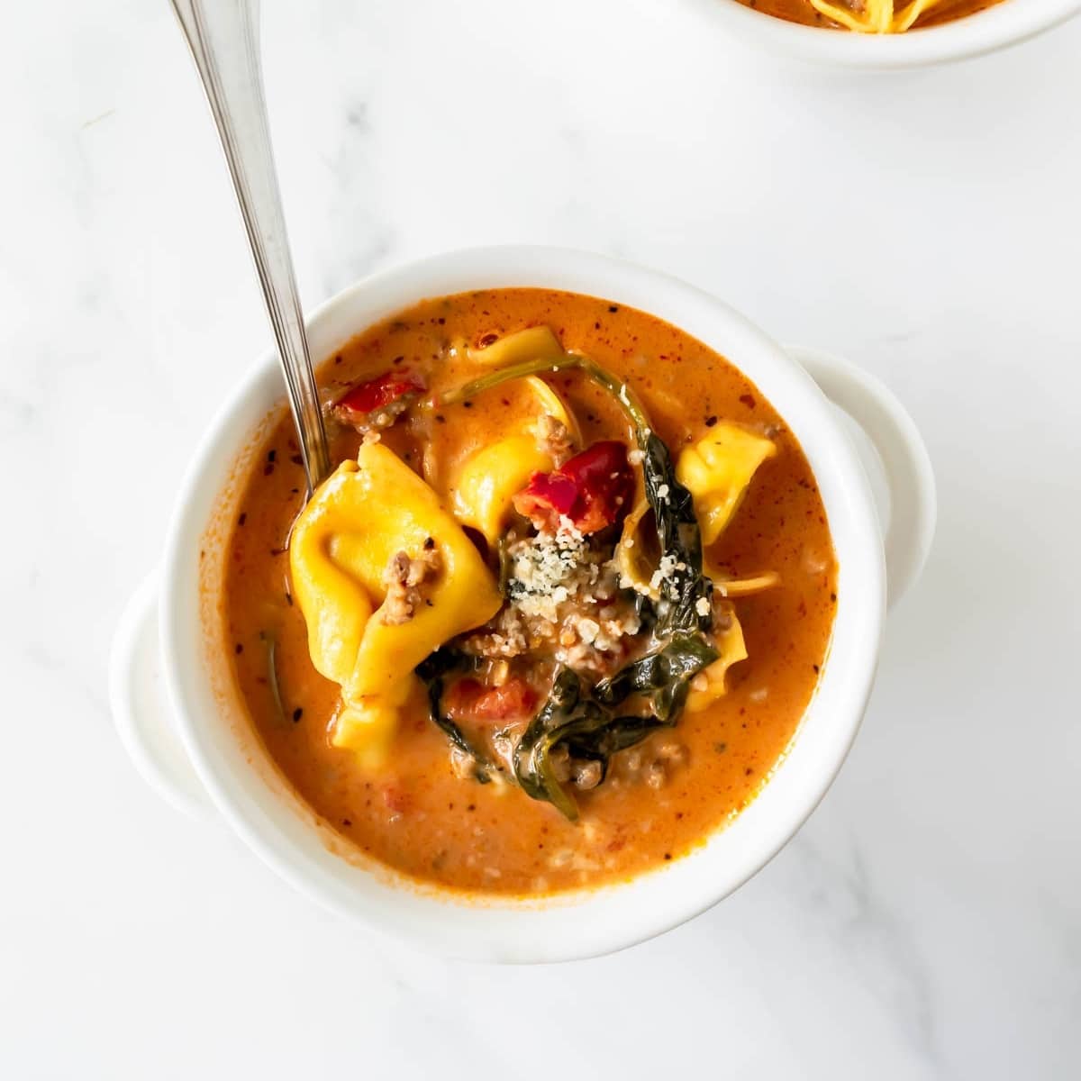 creamy tortellini soup in a white bowl topped with parmesan cheese.