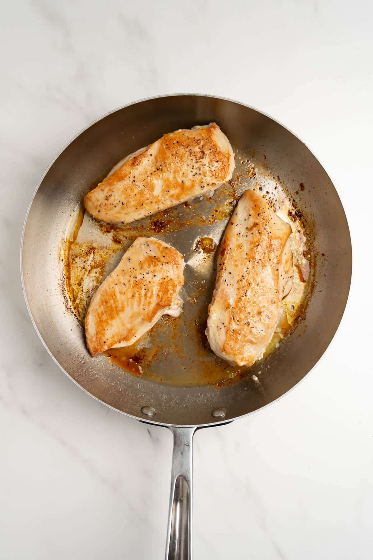 3 pieces of seared chicken in a pan.