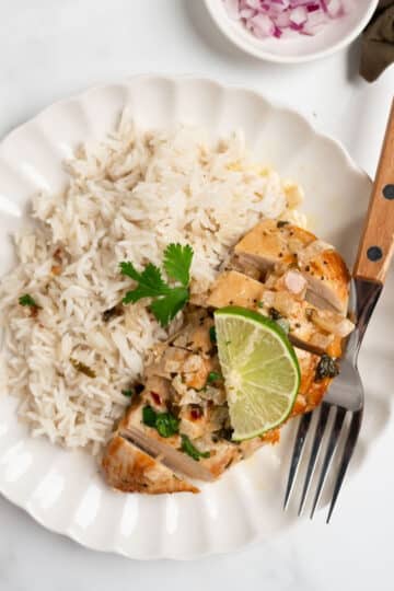 sliced cilantro lime chicken with a cream sauce with rice on a plate with a fork.