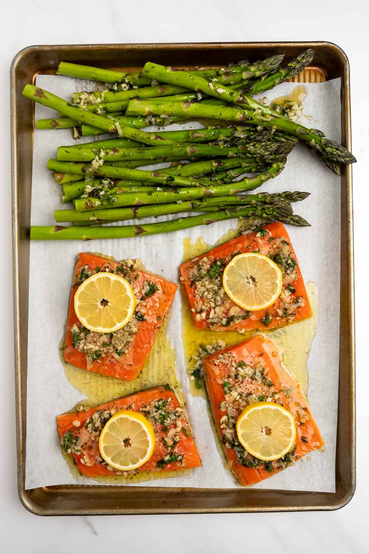 salmon fillets on a baking sheet with marinade and lemon slices.