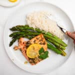 lemon garlic salmon topped with lemon slice on a white plate with rice and asparagus.