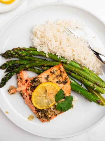 lemon garlic salmon topped with lemon slice on a white plate with rice and asparagus.