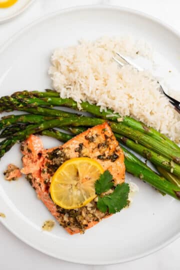 lemon garlic salmon topped with lemon slice on a white plate with rice and asparagus.