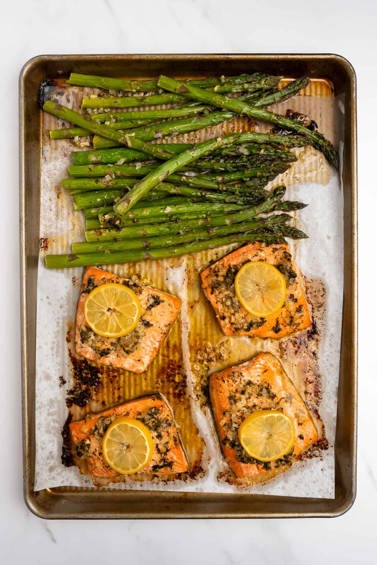 baked salmon fillets on a baking sheet with marinade and lemon slices.