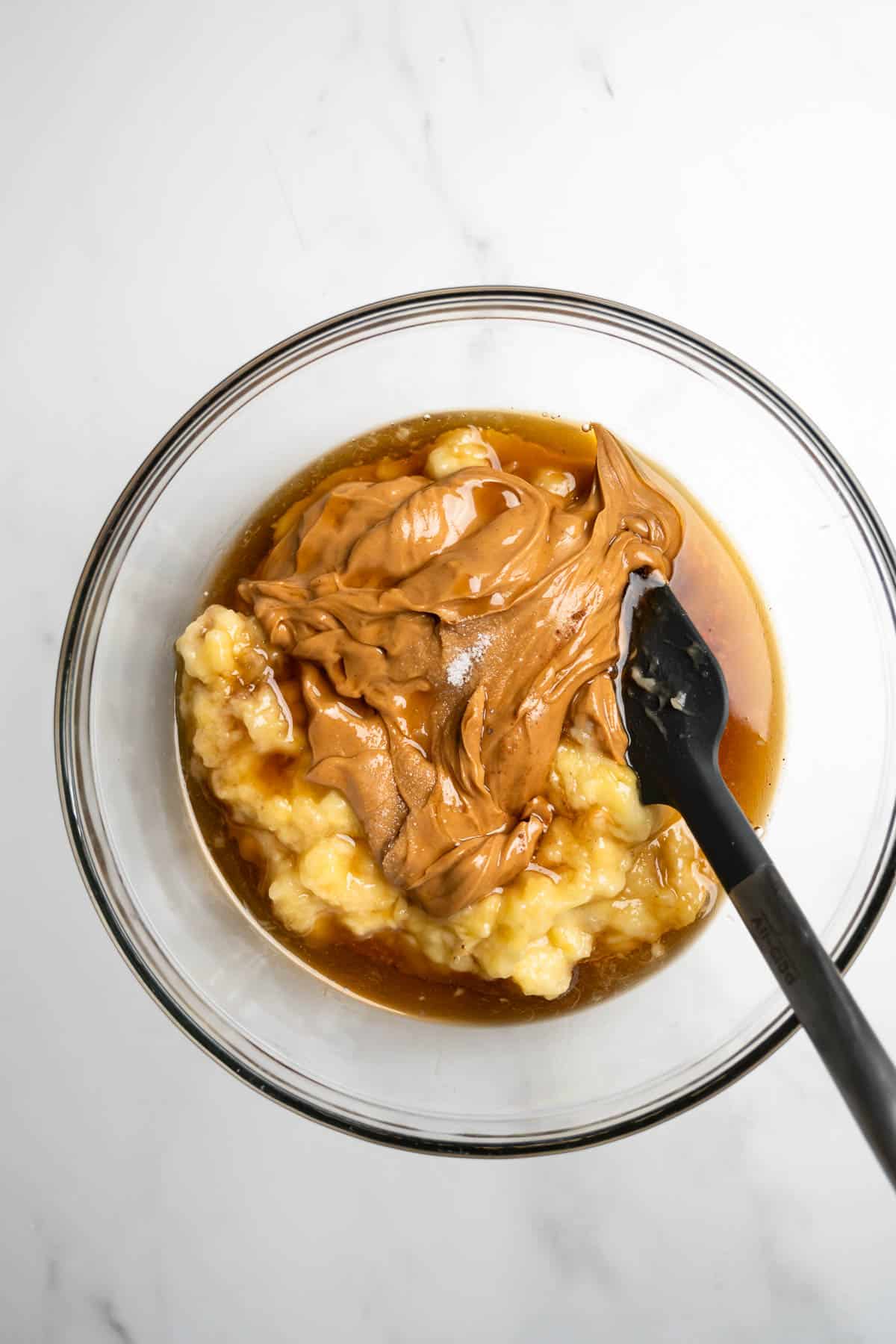 peanut butter and mashed bananas in a glass mixing bowl with a spatula.