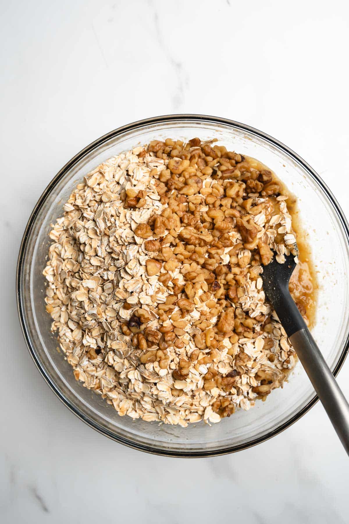 oats and walnuts in a glass mixing bowl with a spatula.