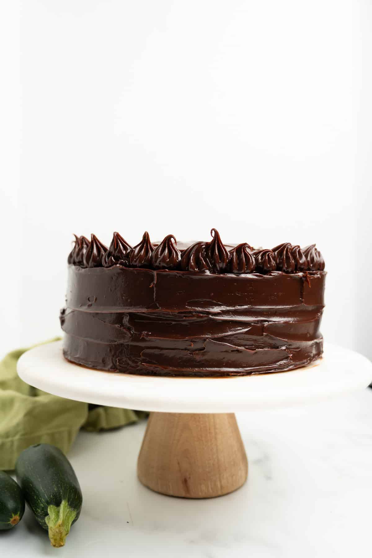 frosted chocolate zucchini cake on a cake stand.