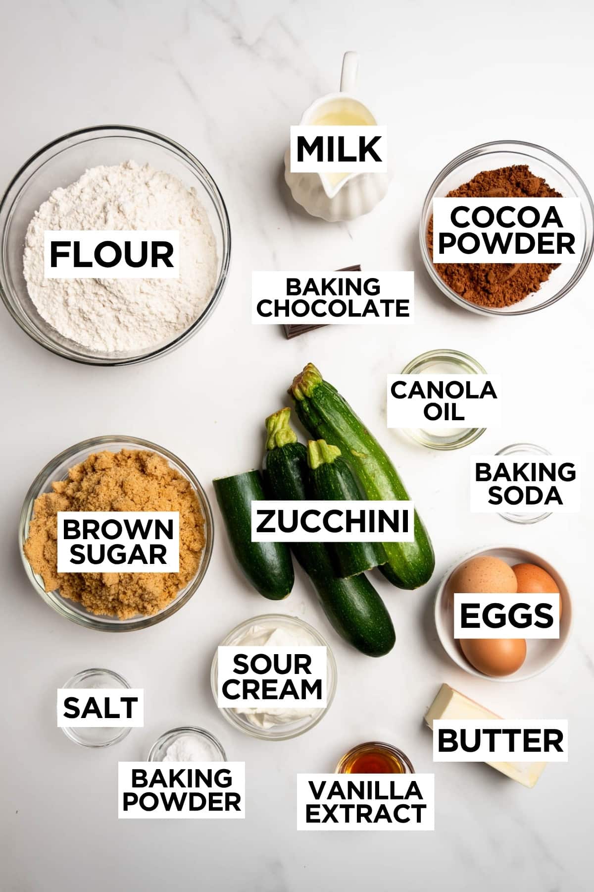 ingredients for chocolate zucchini cake in bowls on a white table with overlay text.