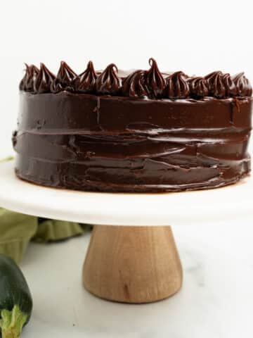frosted chocolate zucchini cake on a cake stand.