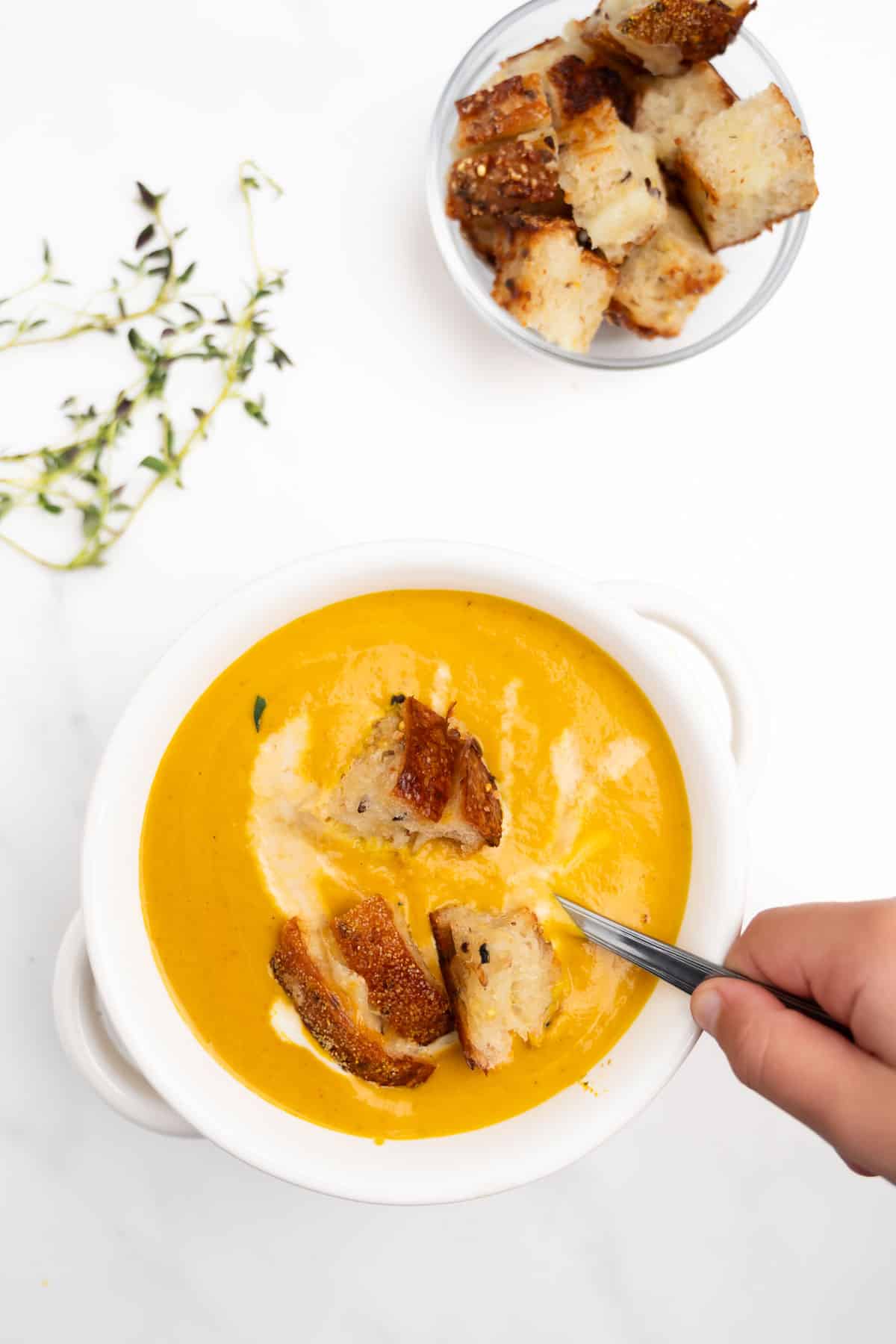pumpkin soup in a bowl with a hand holding a spoon.