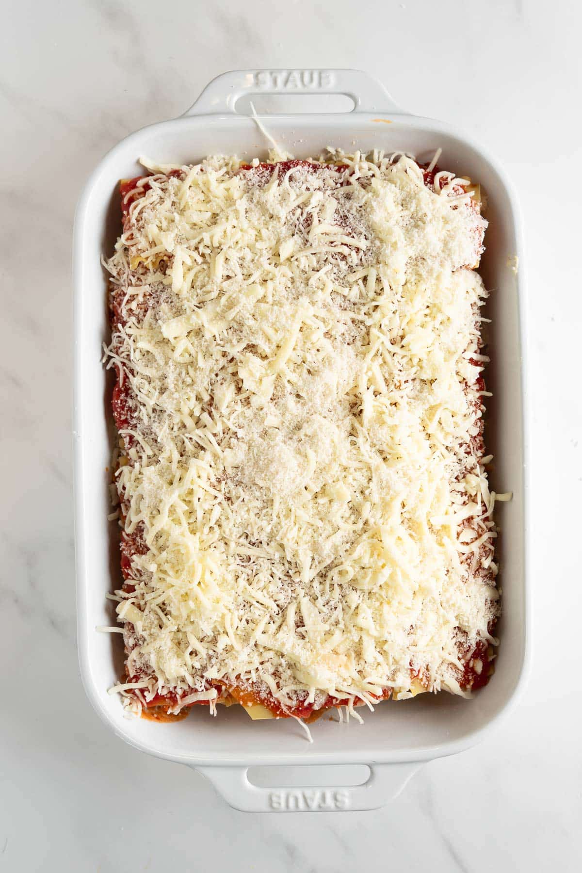 pre-baked lasagna topped with shredded cheese in a baking dish.