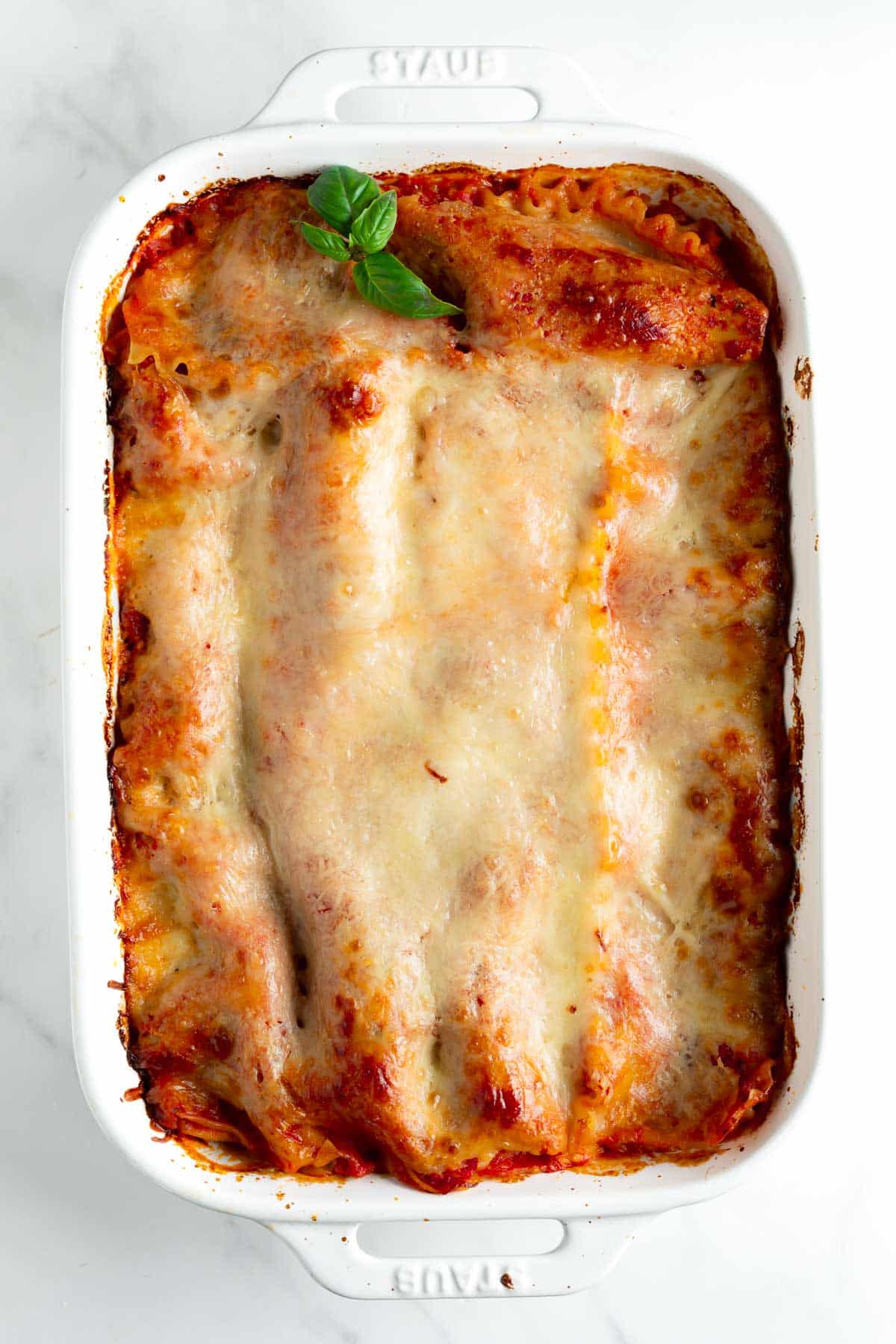 baked lasagna topped with melted cheese and basil in a baking dish.