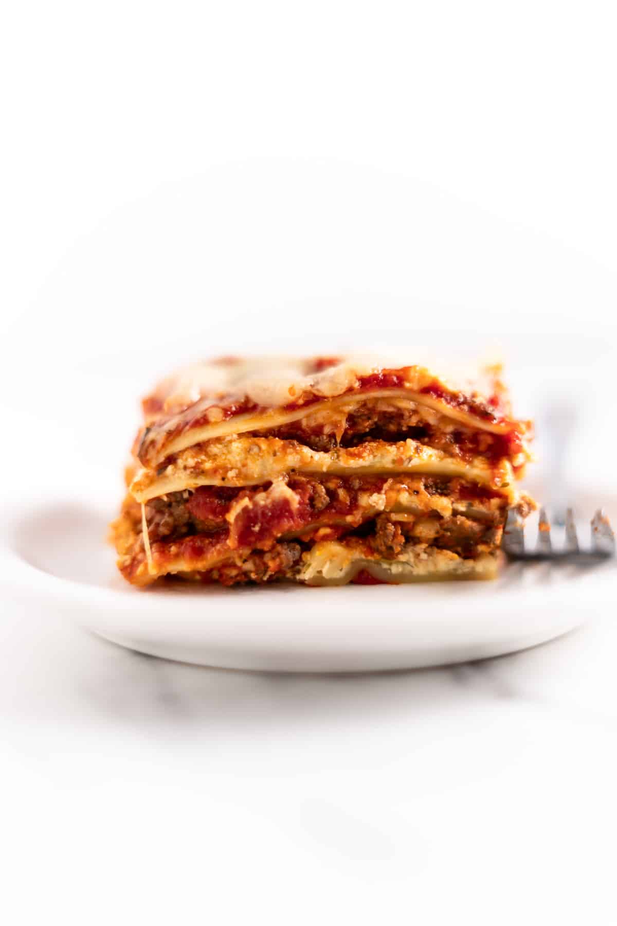 slice of lasagna on a white plate with a fork.
