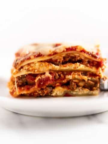 slice of lasagna on a white plate with a fork.