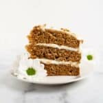 slice of 3 layer carrot cake on a white plate with white flowers.