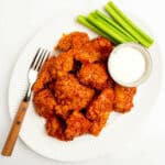 boneless buffalo wings on a platter with celery and blue cheese with a fork.