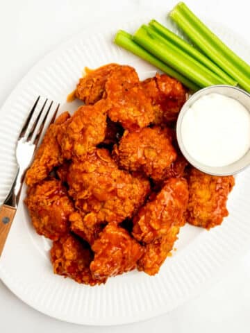 boneless buffalo wings on a platter with celery and blue cheese with a fork.