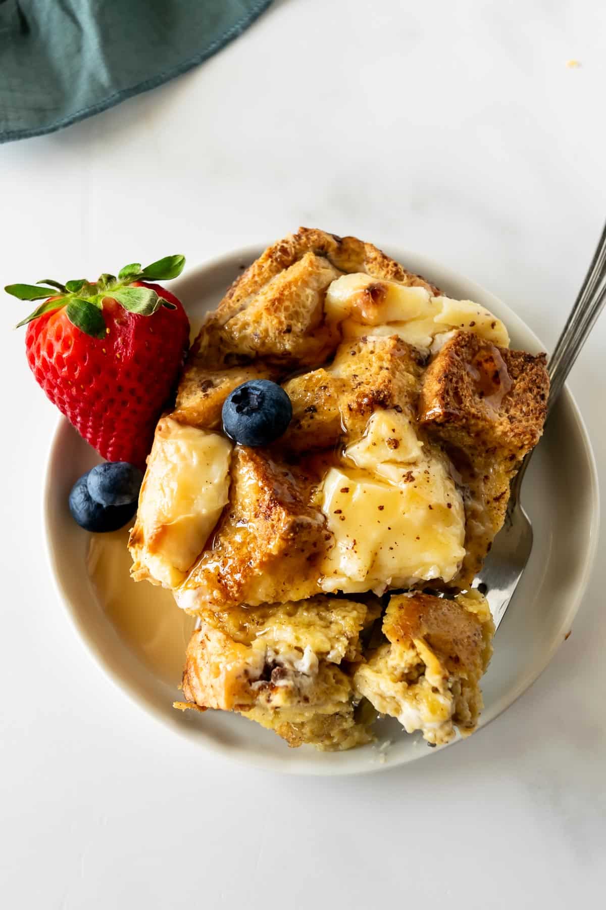 scoop of French toast casserole on a white plate topped with fruit.