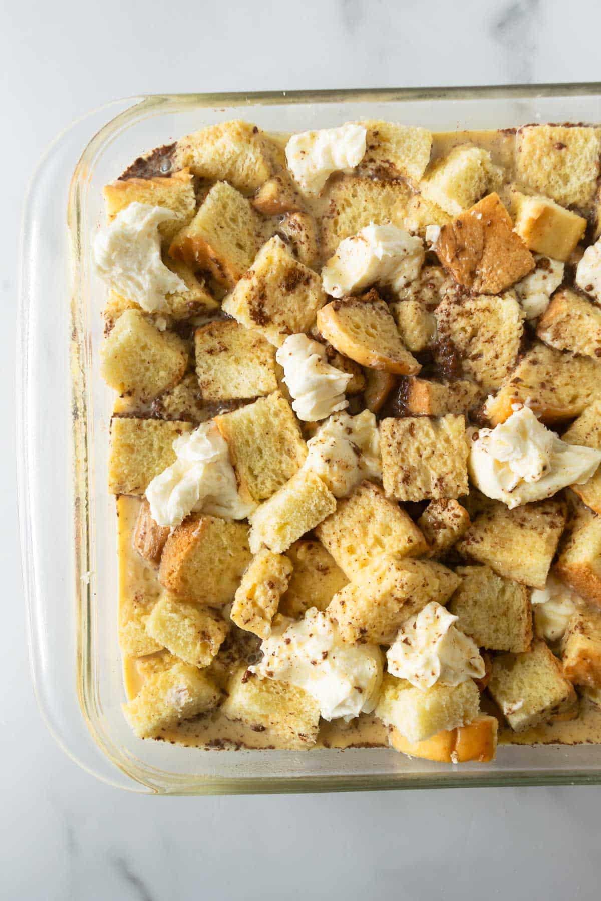 unbaked French toast casserole topped with cream cheese in a baking dish.