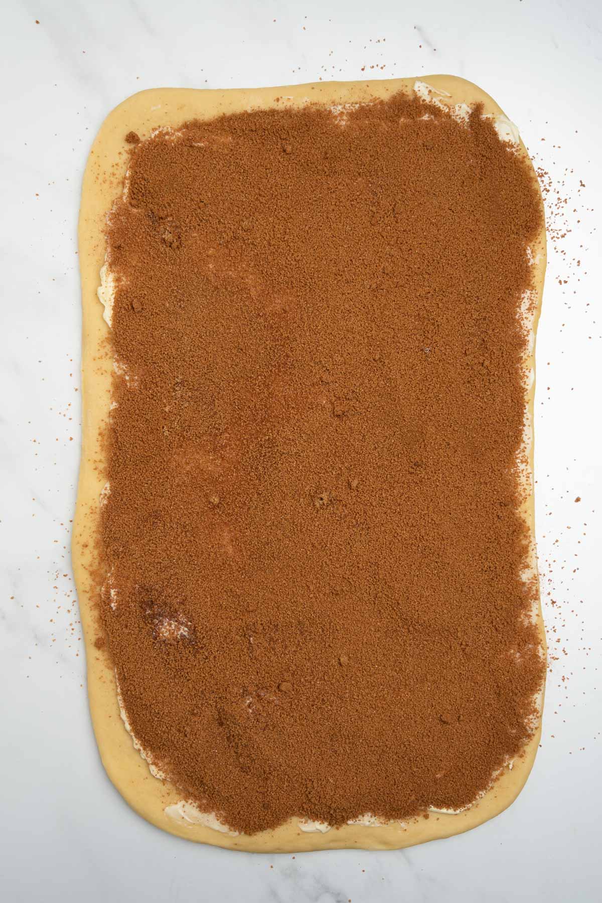 cinnamon roll dough rolled into a rectangle with cinnamon sugar mixture on top.