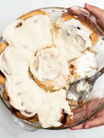 homemade cinnamon rolls in a round baking pan with spoon.