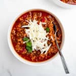 stuffed pepper soup in a bowl topped with shredded cheese with a spoon.