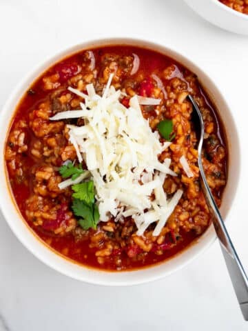 stuffed pepper soup in a bowl topped with shredded cheese with a spoon.