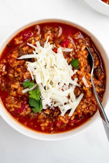 stuffed pepper soup in a bowl topped with shredded cheese with a spoon.