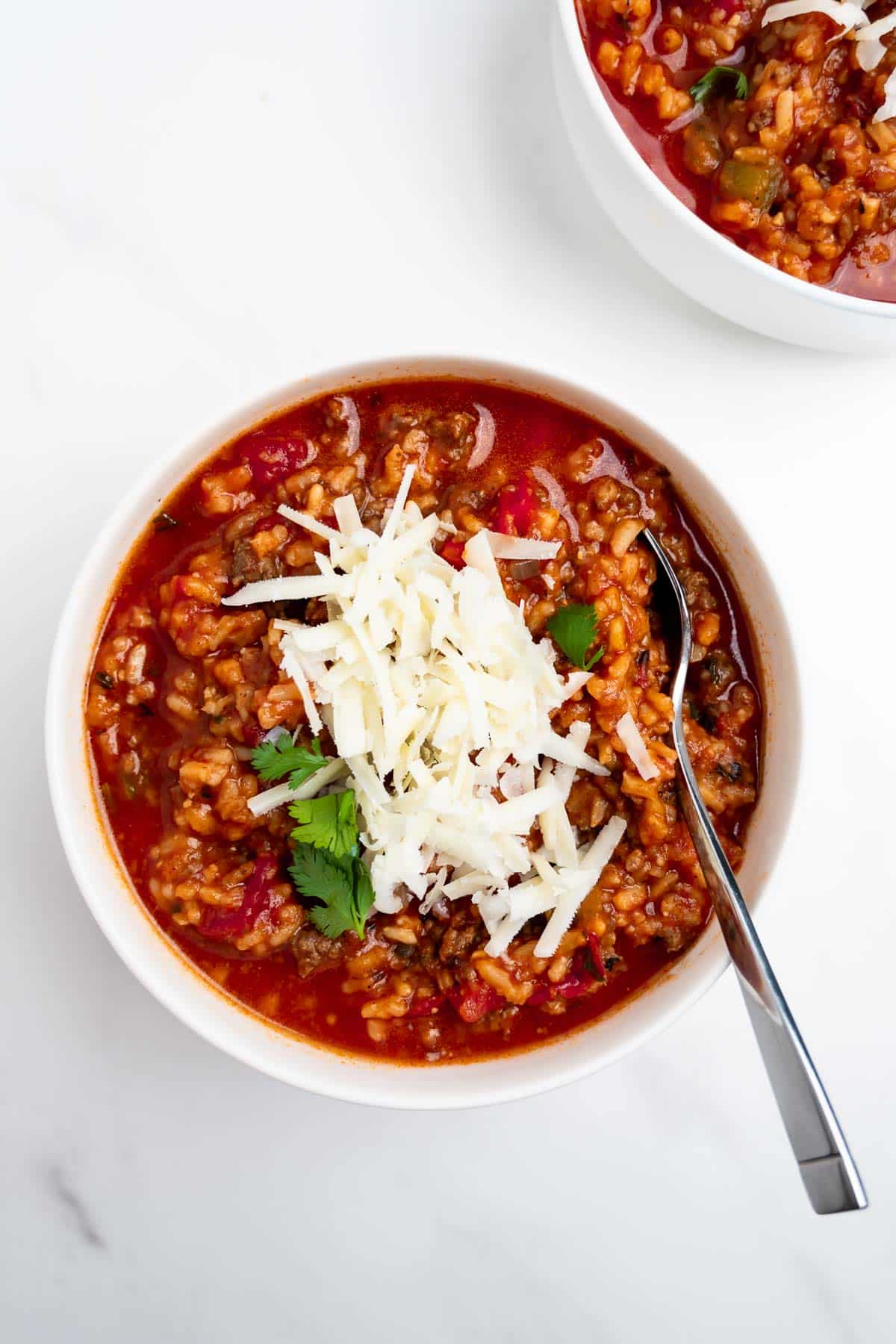 stuffed pepper soup in a bowl topped with shredded cheese and a spoon.