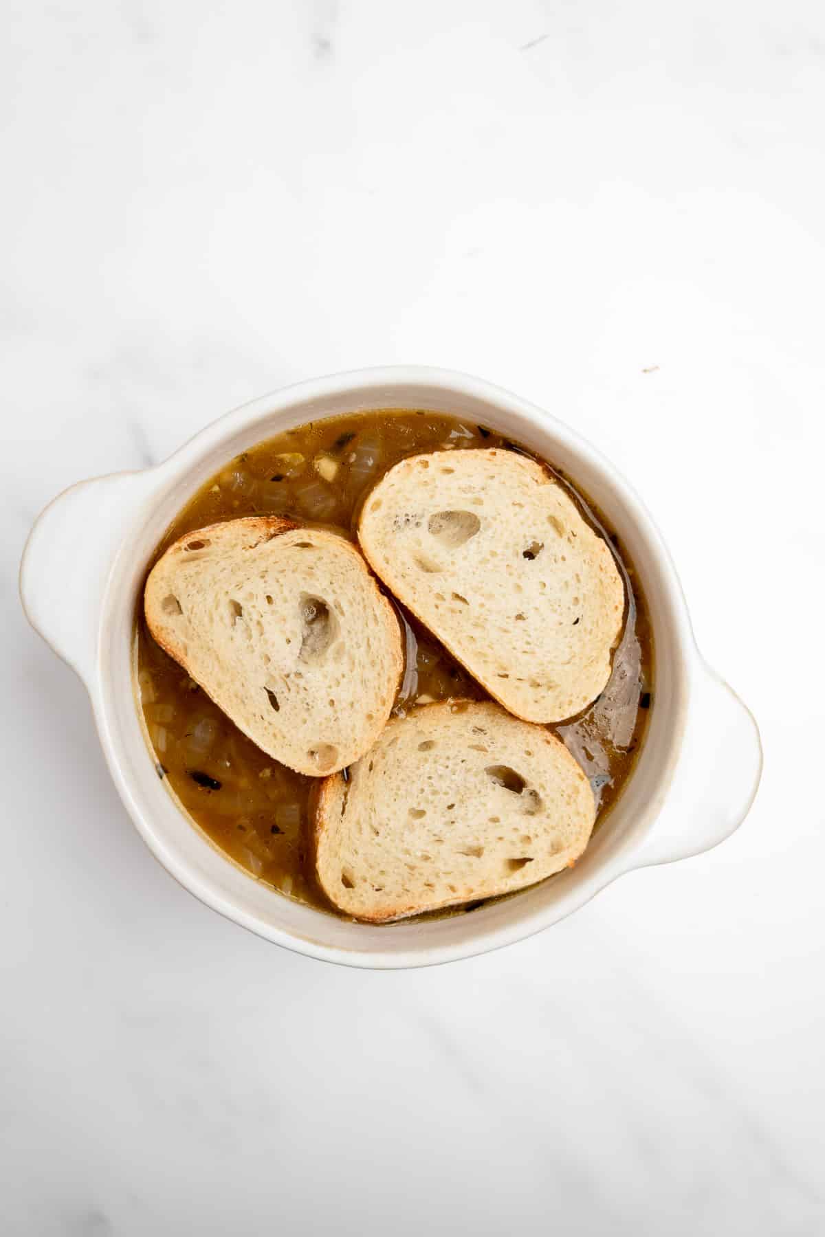 3 slices of bread on top French onion soup in a white bowl.