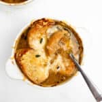 French onion soup in a bowl topped with melted cheese and a spoon.