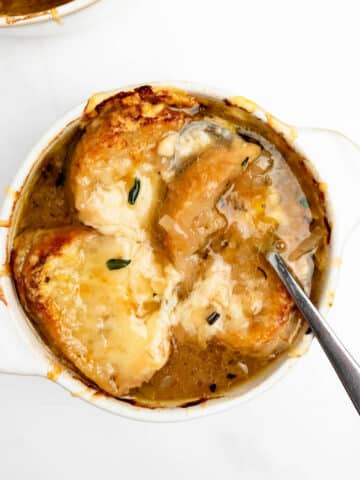 French onion soup in a bowl topped with melted cheese and a spoon.