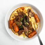 braised short ribs with carrots in a bowl over polenta.