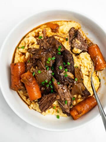 braised short ribs with carrots in a bowl over polenta.