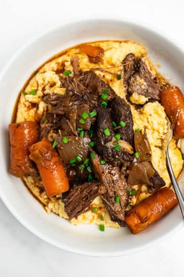 braised short ribs with carrots in a bowl over polenta.