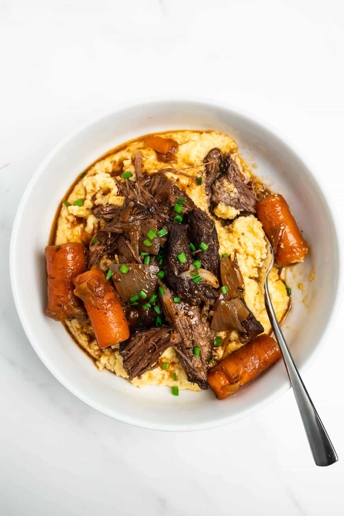 beef short ribs in a bowl with carrots over polenta.