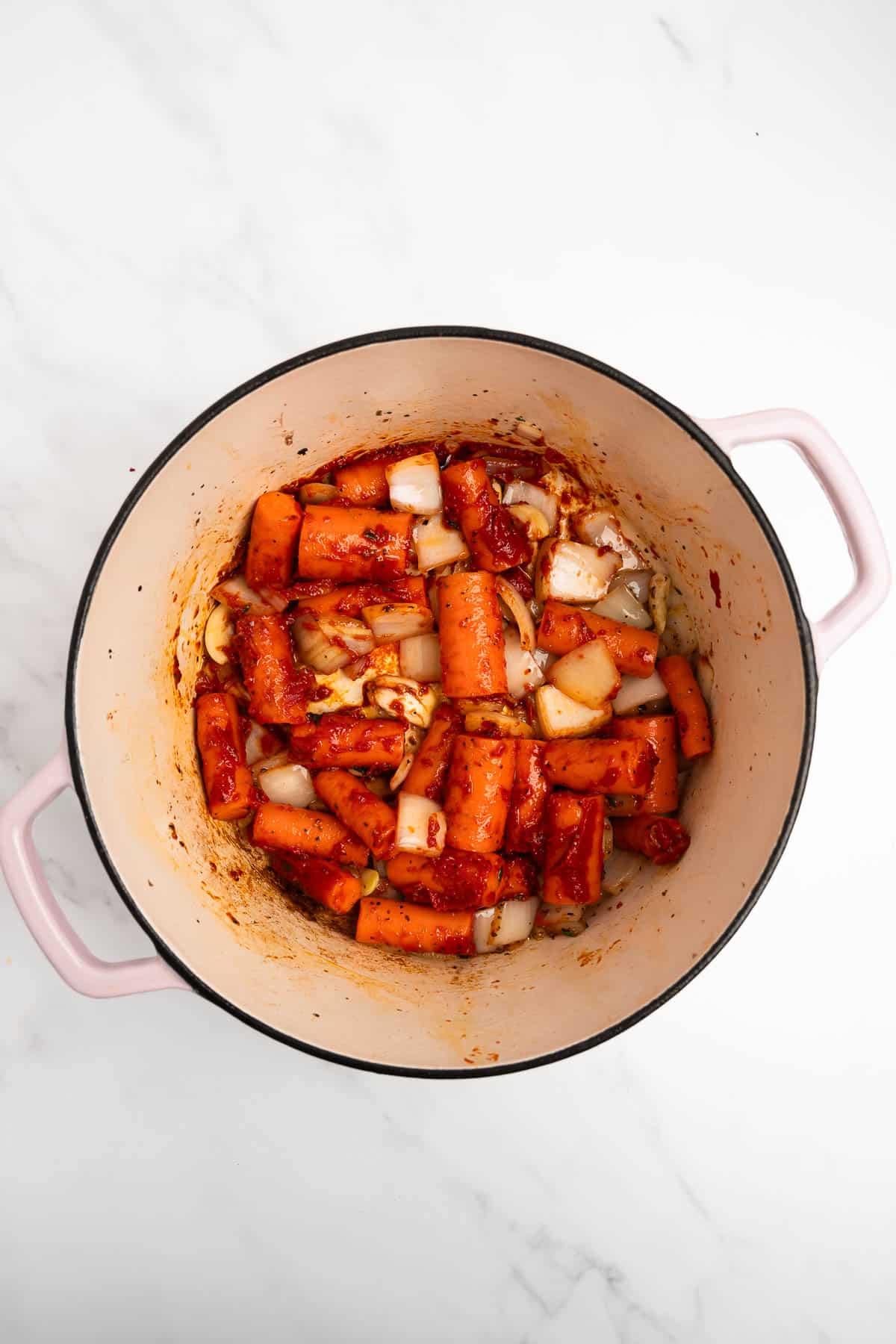 carrots and onion with tomato paste in a pot.